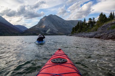 Buzul Gölü 'nde Maceracı Adam Kayağı bulutlu yaz günbatımında güzel Kanada Rocky Dağları ile çevrili. Yukarı Waterton Gölü, Alberta, Kanada.