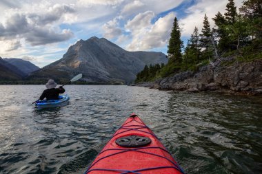 Buzul Gölü 'nde Maceracı Adam Kayağı bulutlu yaz günbatımında güzel Kanada Rocky Dağları ile çevrili. Yukarı Waterton Gölü, Alberta, Kanada.