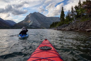 Buzul Gölü 'nde Maceracı Adam Kayağı bulutlu yaz günbatımında güzel Kanada Rocky Dağları ile çevrili. Yukarı Waterton Gölü, Alberta, Kanada.