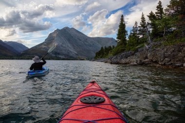 Buzul Gölü 'nde Maceracı Adam Kayağı bulutlu yaz günbatımında güzel Kanada Rocky Dağları ile çevrili. Yukarı Waterton Gölü, Alberta, Kanada.