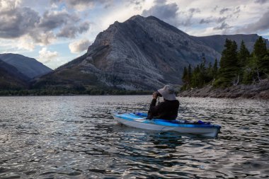 Buzul Gölü 'nde Maceracı Adam Kayağı bulutlu yaz günbatımında güzel Kanada Rocky Dağları ile çevrili. Yukarı Waterton Gölü, Alberta, Kanada.