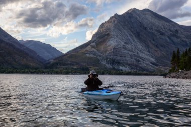 Buzul Gölü 'nde Maceracı Adam Kayağı bulutlu yaz günbatımında güzel Kanada Rocky Dağları ile çevrili. Yukarı Waterton Gölü, Alberta, Kanada.