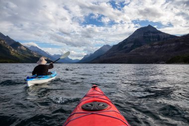Buzul Gölü 'nde Maceracı Adam Kayağı bulutlu yaz günbatımında güzel Kanada Rocky Dağları ile çevrili. Yukarı Waterton Gölü, Alberta, Kanada.