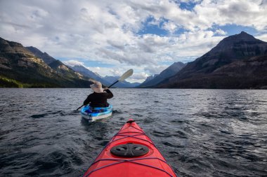 Buzul Gölü 'nde Maceracı Adam Kayağı bulutlu yaz günbatımında güzel Kanada Rocky Dağları ile çevrili. Yukarı Waterton Gölü, Alberta, Kanada.
