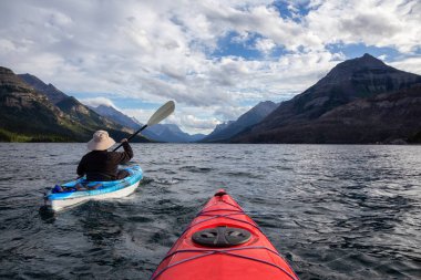 Buzul Gölü 'nde Maceracı Adam Kayağı bulutlu yaz günbatımında güzel Kanada Rocky Dağları ile çevrili. Yukarı Waterton Gölü, Alberta, Kanada.