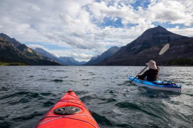 Buzul Gölü 'nde Maceracı Adam Kayağı bulutlu yaz günbatımında güzel Kanada Rocky Dağları ile çevrili. Yukarı Waterton Gölü, Alberta, Kanada.