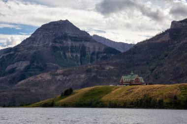 Buzul Gölü 'ndeki Iconic Oteli bulutlu yaz günbatımında Kanada Rocky Dağları ile çevrilidir. Yukarı Waterton Gölü, Alberta, Kanada.