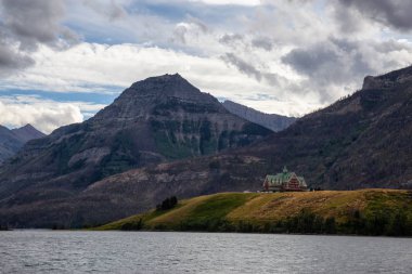 Buzul Gölü 'ndeki Iconic Oteli bulutlu yaz günbatımında Kanada Rocky Dağları ile çevrilidir. Yukarı Waterton Gölü, Alberta, Kanada.