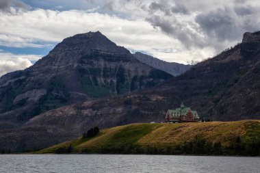 Buzul Gölü 'ndeki Iconic Oteli bulutlu yaz günbatımında Kanada Rocky Dağları ile çevrilidir. Yukarı Waterton Gölü, Alberta, Kanada.