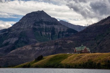 Buzul Gölü 'ndeki Iconic Oteli bulutlu yaz günbatımında Kanada Rocky Dağları ile çevrilidir. Yukarı Waterton Gölü, Alberta, Kanada.