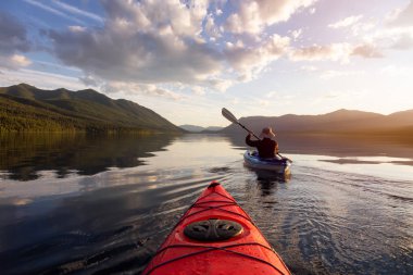 Maceraperest Adam McDonald Gölü 'nde güneşli bir yaz akşamında arka planda Amerikan Rocky Dağları ile kayak yapıyor. Buzul Ulusal Parkı, Montana, ABD 'de çekildi..