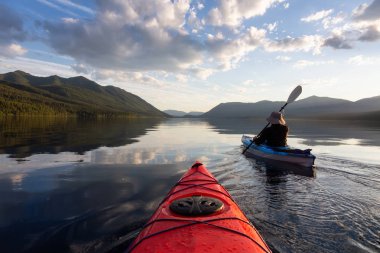 Maceraperest Adam McDonald Gölü 'nde güneşli bir yaz akşamında arka planda Amerikan Rocky Dağları ile kayak yapıyor. Buzul Ulusal Parkı, Montana, ABD 'de çekildi..