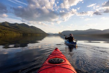 Maceraperest Adam McDonald Gölü 'nde güneşli bir yaz akşamında arka planda Amerikan Rocky Dağları ile kayak yapıyor. Buzul Ulusal Parkı, Montana, ABD 'de çekildi..
