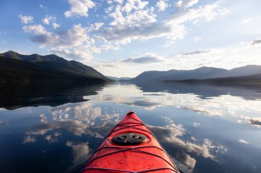 Kayaking in Lake McDonald during a sunny summer sunset with American Rocky Mountains in the background. Taken in Glacier National Park, Montana, USA. clipart