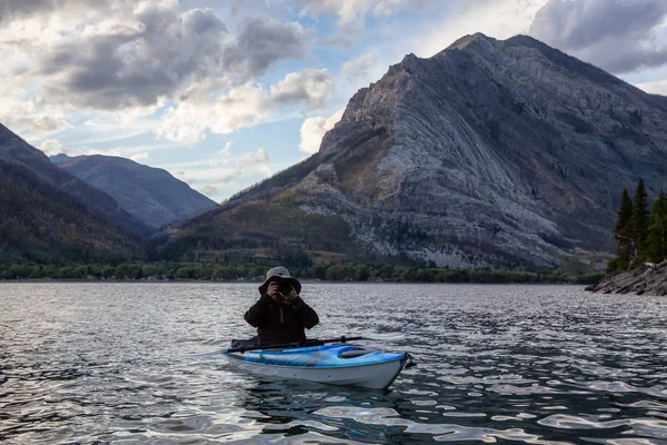 Buzul Gölü 'nde Maceracı Adam Kayağı bulutlu yaz günbatımında güzel Kanada Rocky Dağları ile çevrili. Yukarı Waterton Gölü, Alberta, Kanada.