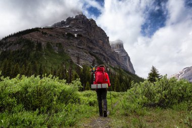 Bulutlu bir günde Kanada Kayalıklarında Kadın Sırt Çantası Yürüyüşü.