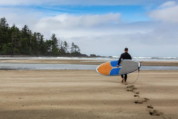 Сёрфер в гидрокостюме идет по песчаному пляжу с доской для серфинга — стоковое фото