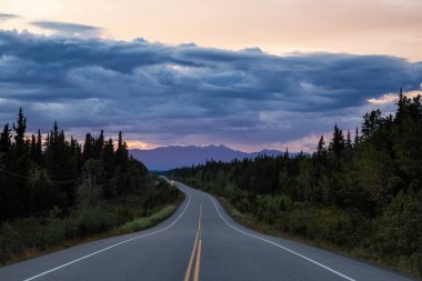 Güzel manzaralı bir yol manzarası, Alaska Hwy, Kuzey Kayalıklarında dramatik bulutlu bir günbatımında.