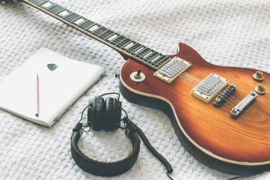 Beyaz bir battaniye ile bir dizüstü bilgisayar ve kulaklık üzerinde elektro gitar modelidir
