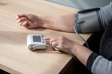 Kadın kendi kendine kan basıncını evde ölçüyor, elini yakın plan çekiyor..