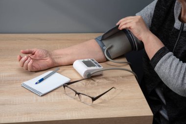 Kadın evde kan basıncını bağımsız olarak ölçer ve ölçümleri bir deftere kaydeder.