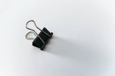 Gümüş saplı siyah klasör temiz beyaz bir yüzeye uzanıyor, sağa doğru uzun bir gölge bırakıyor..