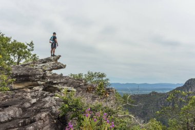 Young adult standing on rocky edge with beautiful natural cerrado landscape on the background, Mirante da Janela hike, Chapada dos Veadeiros, Goias, central Brazil clipart