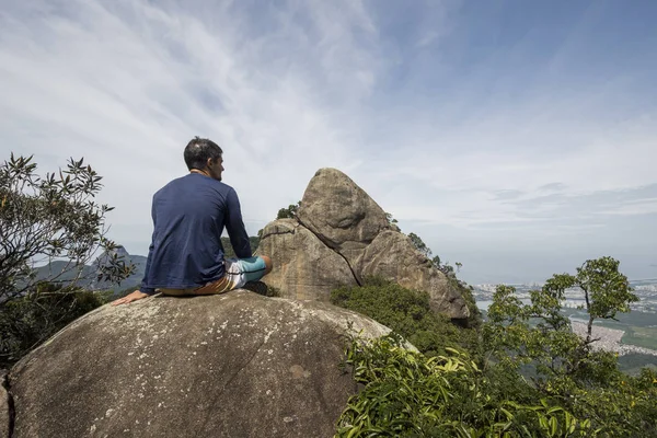 大西洋熱帯雨林 ティジュカ フォレスト国立公園 ジャネイロ ブラジルの緑の山々 に美しい景観を持つ岩が多い峰の上に座っている若い男 — ストック写真