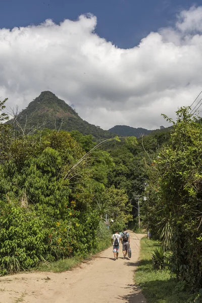 Friends hiking on dirt path with green rainforest on the back, Ilha Grande, Costa Verde, south Rio de Janeiro, Brazil