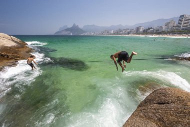 Genç adam Arpoador Beach rock kristal berraklığında su ve dağların güzel manzara arkasında güneşli bir günde, Rio de Janeiro, Brezilya atlama