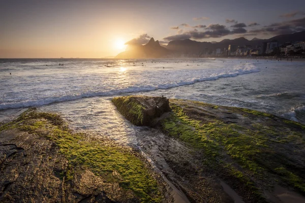 Beautiful sunset landscape by the ocean rocks with mountains on the back, Ipanema Beach, Rio de Janeiro, Brazil