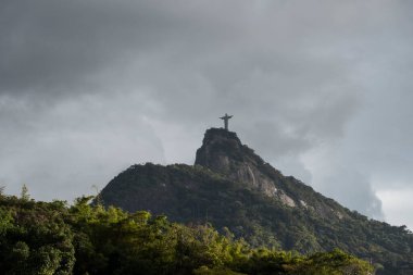 Gökyüzünde ağır gri bulutlar olan yeşil dağın tepesindeki Kurtarıcı İsa heykeli Rio de Janeiro, Brezilya