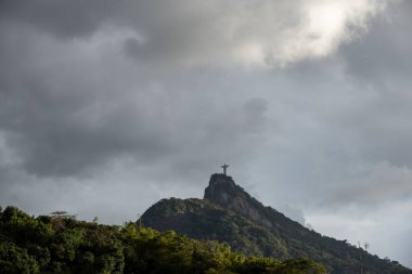 Gökyüzünde ağır gri bulutlar olan yeşil dağın tepesindeki Kurtarıcı İsa heykeli Rio de Janeiro, Brezilya