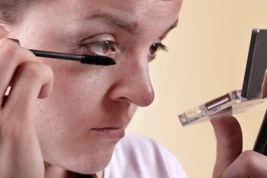 Kız aynaya baktı ve bir kirpik fırçası tuttu. Kız kirpikleri boyuyor.