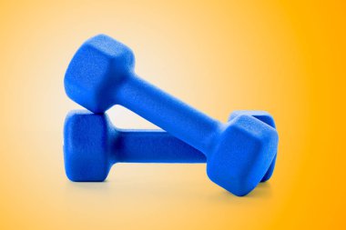 İki küçük mavi dumbbells parlak turuncu arka plana, yakın çekim ve açık görünüm