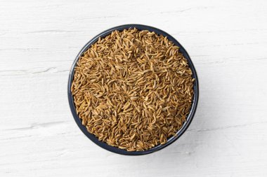 Kimyon tohumu beyaz ahşap zemin üzerinde yuvarlak kase görüntülemek doğrudan yukarıda.