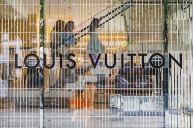 Louis Vuitton mağazası vitrininde logo ve içinde müşteriler var.