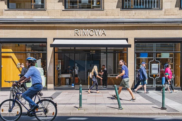Rimowa lüks bavullar mağaza vitrininde logo levhası olan bir mağaza ve oradan geçen insanlar.