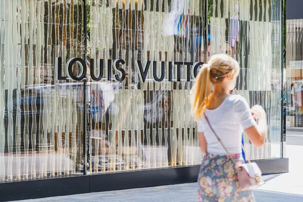 İnsanlar vitrininde logo olan modern Louis Vuitton mağazasının önünden geçiyorlar.