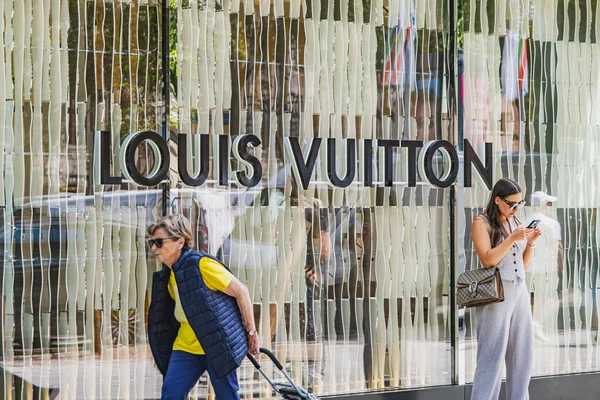 İnsanlar vitrininde logo olan modern Louis Vuitton mağazasının önünden geçiyorlar.