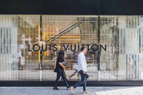 İnsanlar vitrininde logo olan modern Louis Vuitton mağazasının önünden geçiyorlar.