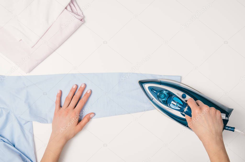 Woman hand with iron ironing clothes, top view