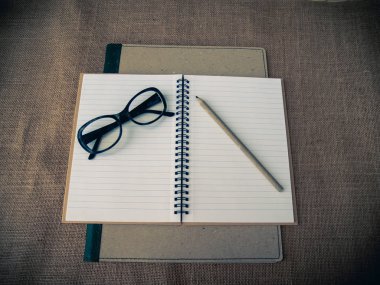 Vintage tarzı. Binder, açık defter, gözüne gözlük, kalemler ve çuval bezi arka plan ile organize masası