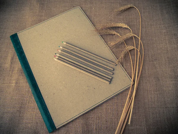 Vintage style. Organized desk with binder, pencils and dry wheat and burlap background