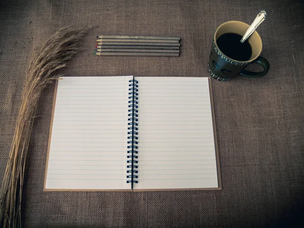 ビンテージ スタイルです ノートブックを開く 乾いた草 一杯のコーヒー 黄麻布背景と机が整理されて — ストック写真