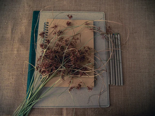 Vintage style. Organized desk with binder, closed notebook, pencils, dry grass and burlap background