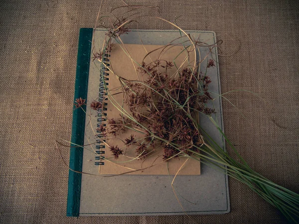 Vintage style. Organized desk with binder, closed notebook, dry grass and burlap background