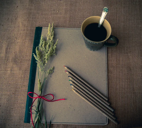 Vintage style. Organized desk with binder, a cup of coffee, dry grass, pencils and burlap background