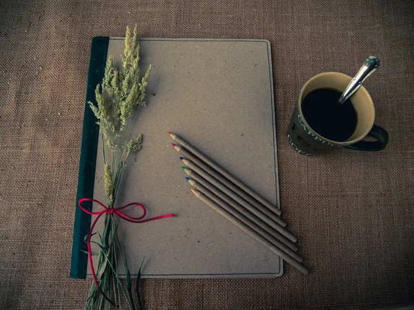 Vintage style. Organized desk with binder, a cup of coffee, dry grass, pencils and burlap background
