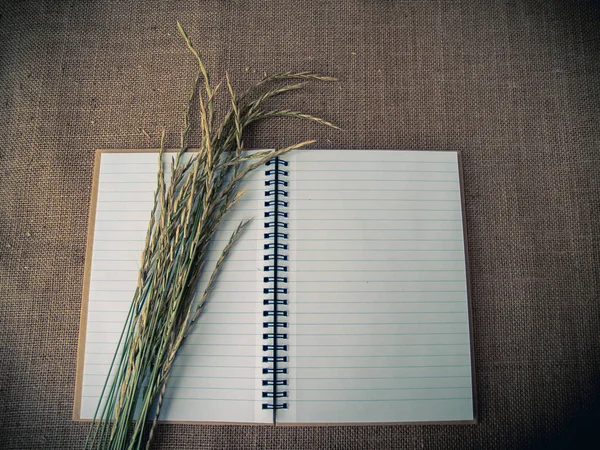 Vintage style. Organized desk with open notebook, dry grass and burlap background